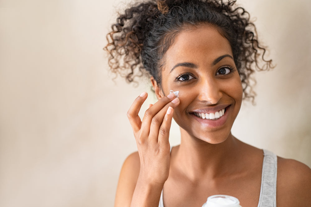 African woman smiling and applying moisturiser